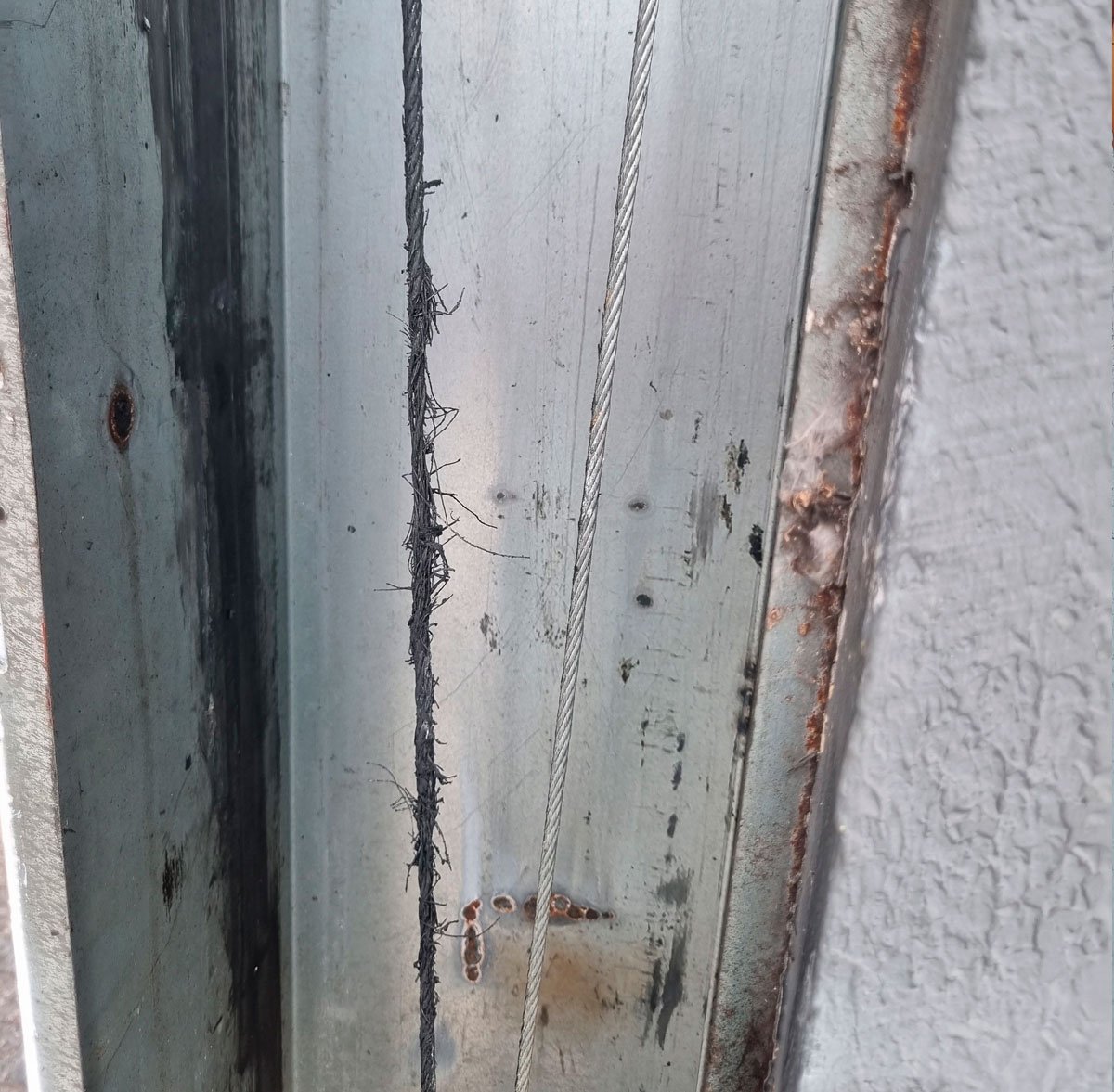 Portão basculante com cabo de aço desfiado saindo do centro da roldana — necessidade de troca imediata